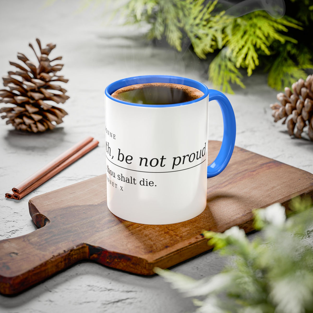 Death Be Not Proud mug with a blue handle styled on a board with pine cones and cinnamon